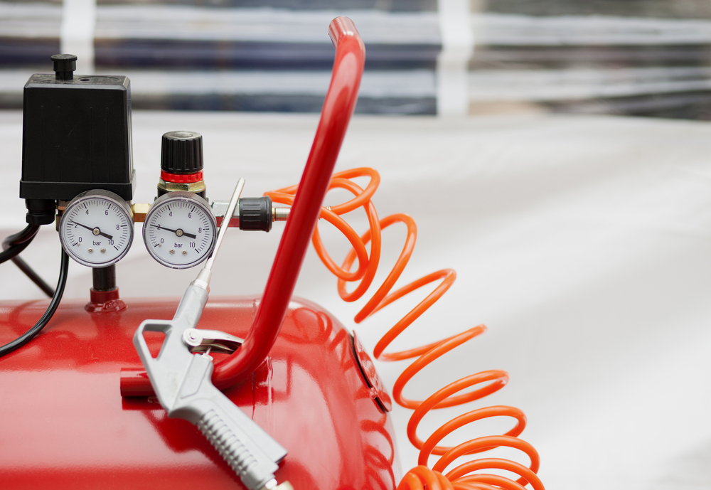 red air compressor with gauges connected to a hose and air tool