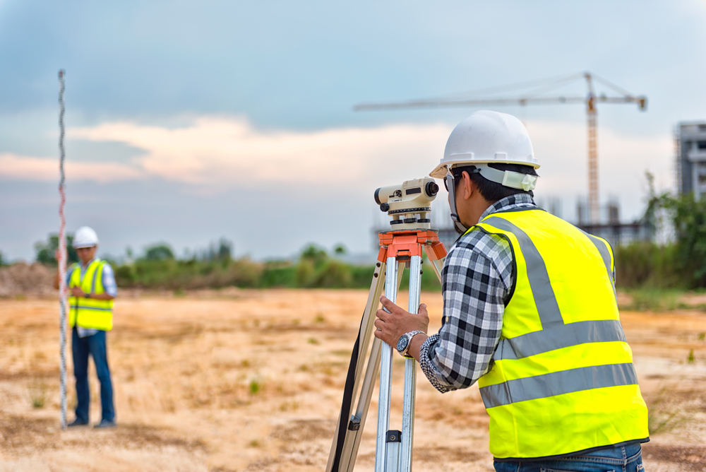 two men in yellow vests and white hard hats surveying an empty lot