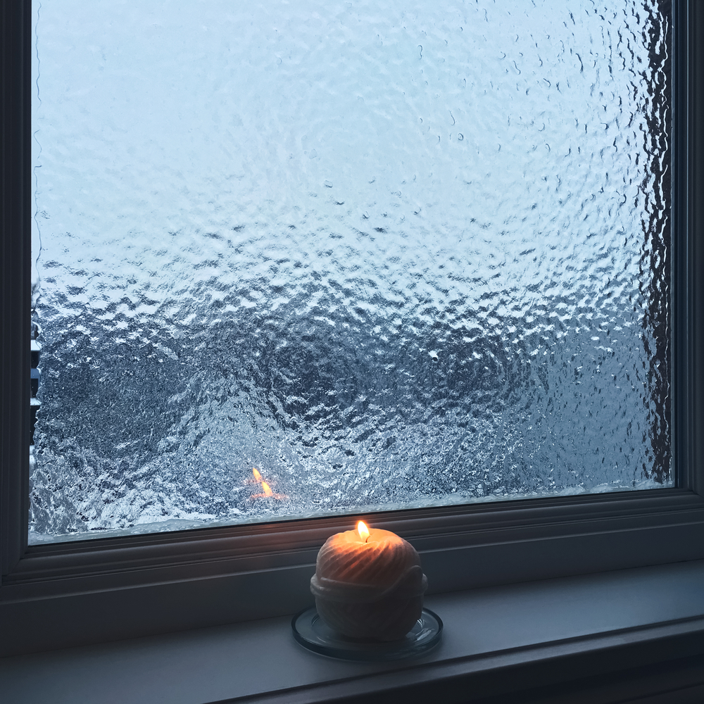 Lit candle next to frosted window