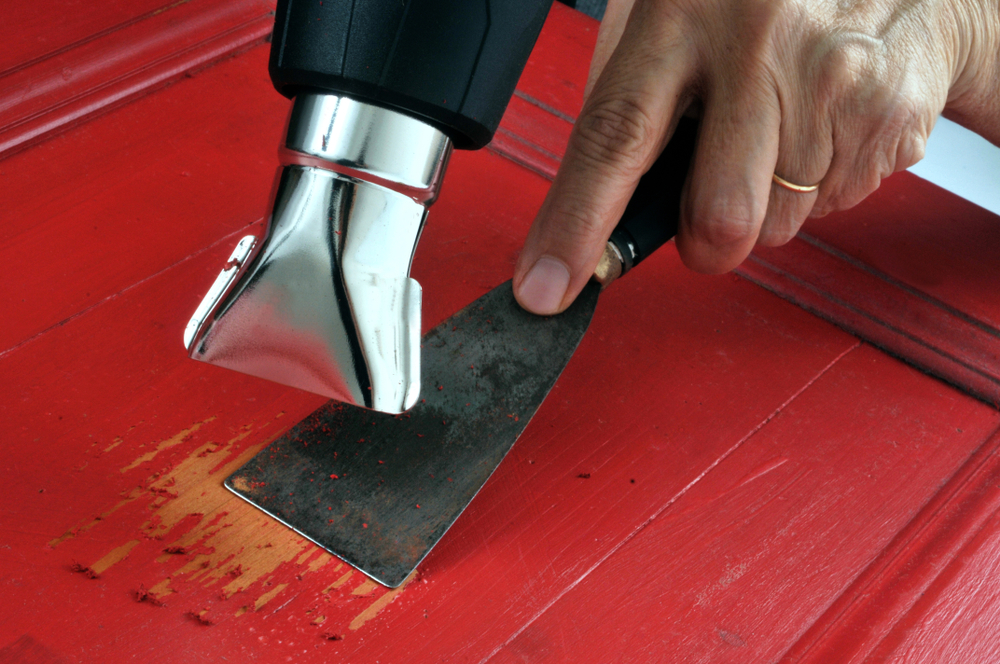 A worker removing paint from wood with a heat gun and spatula