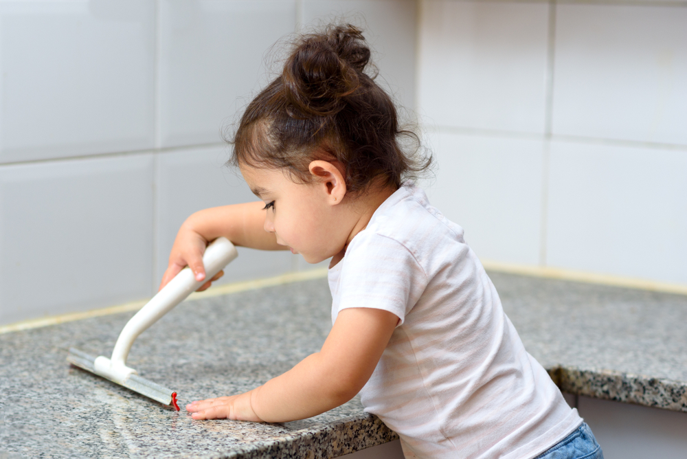 Toddler uses squeegee on granite counter