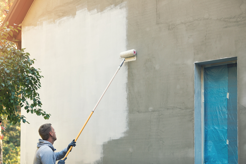 a man paints the exterior walls of a house with a long roller
