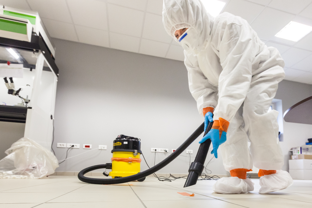 a person in protective clothing and gear using a HEPA vacuum to vacuum the floor