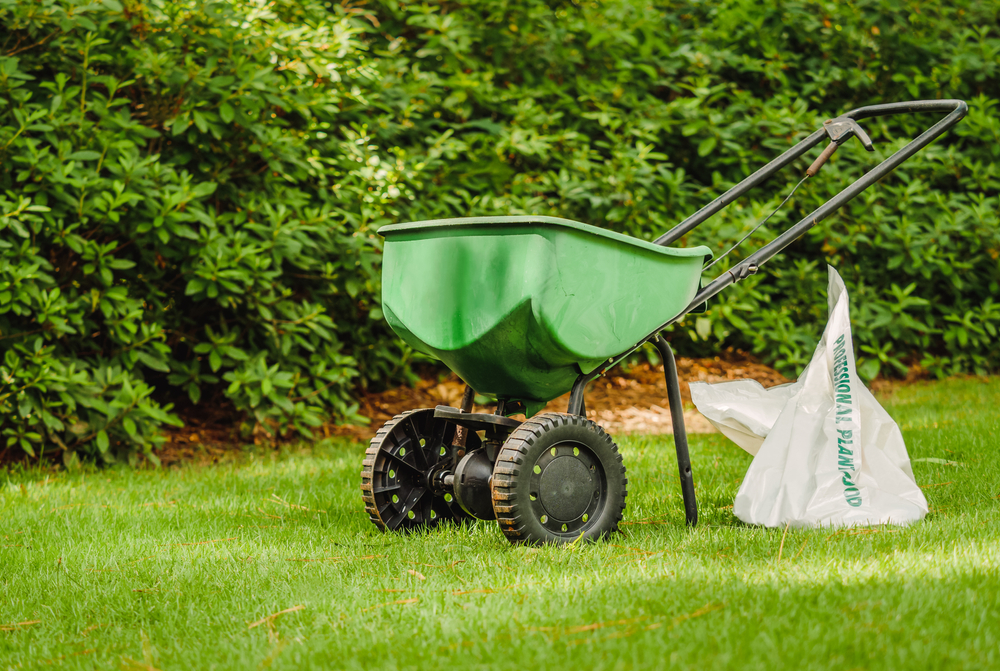 fertilizer spreader resting on lawn with bag of fertilizer