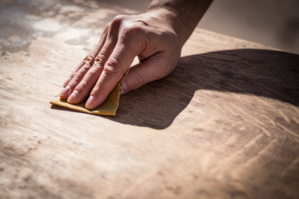 hand sanding a wooden tabletop using sandpaper