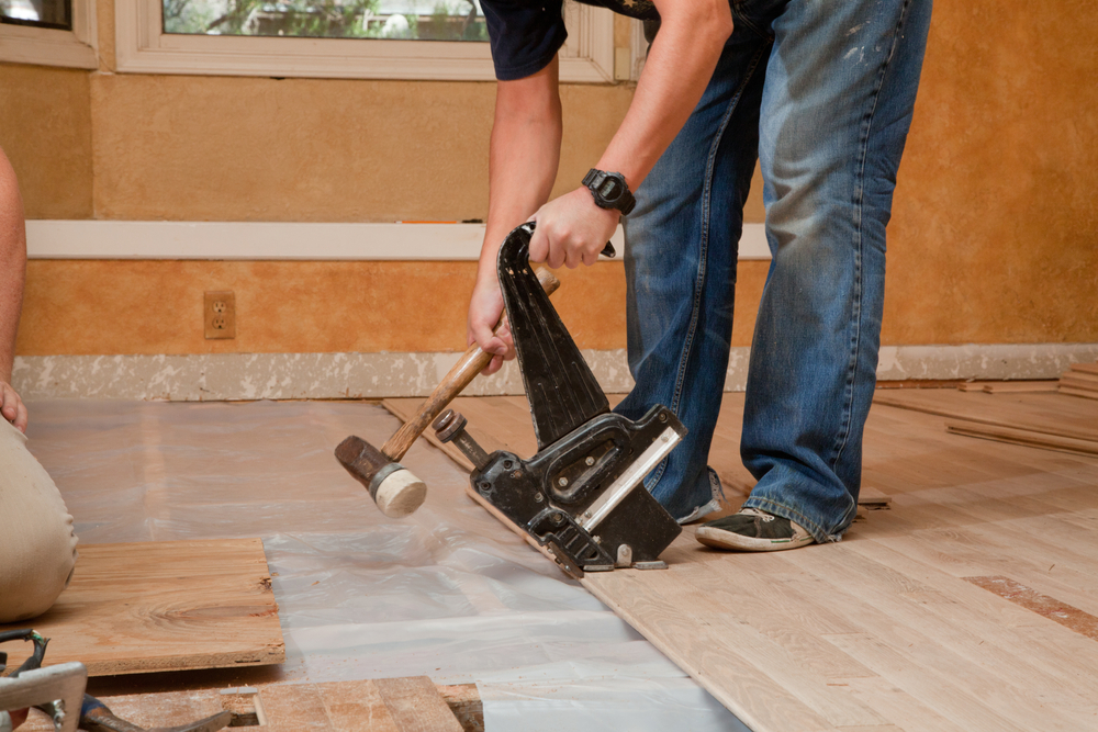 laborer installing wood flooring with a pneumatic nailer