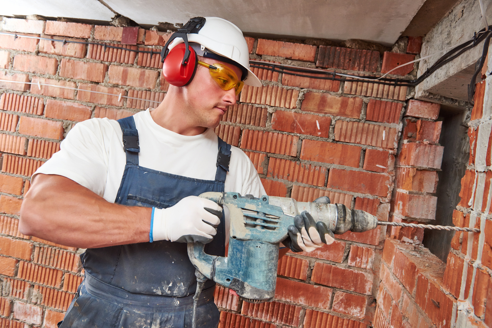 worker using hammer drill on brick