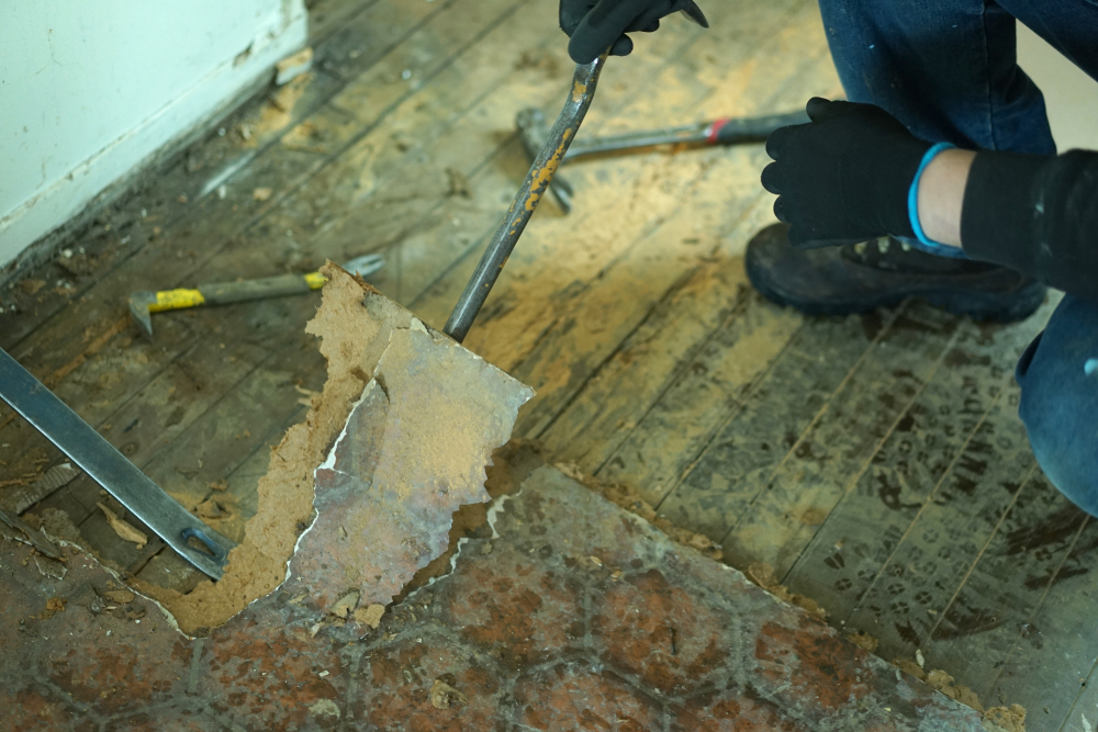 person removing linoleum piece by piece from hardwood subfloor with a crowbar