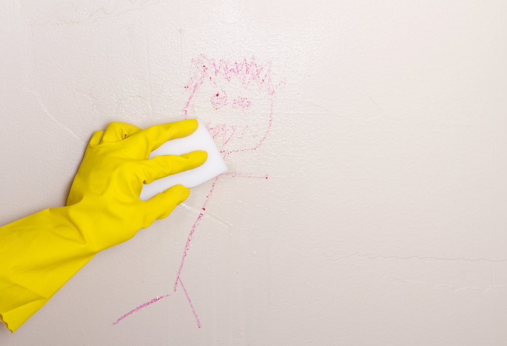 a gloved hand cleans a crayon stick figure off the wall with a sponge