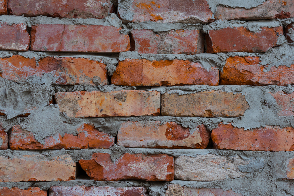 close-up of an old brick wall with damaged bricks and crumbling grey mortar